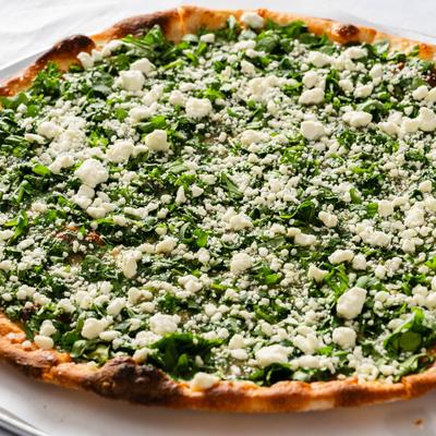Spinach pizza topped with crumbled cheese.