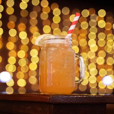 Peach Drink served in a mason jar, on a table with bokeh of lights in the background.