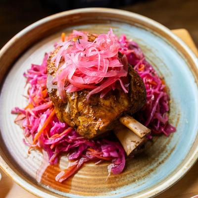 Top-down view of braised pork shank with spicy red slaw and pickled onions on top.