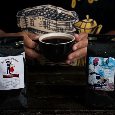 Hands holding a coffee cup alongside two bags of coffee beans.