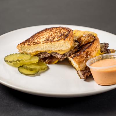 Smashburger Grilled Cheese sandwich served with a dipping sauce and pickle slices.