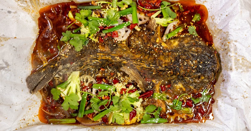 Whole grilled fish topped with chilies, herbs, and vegetables