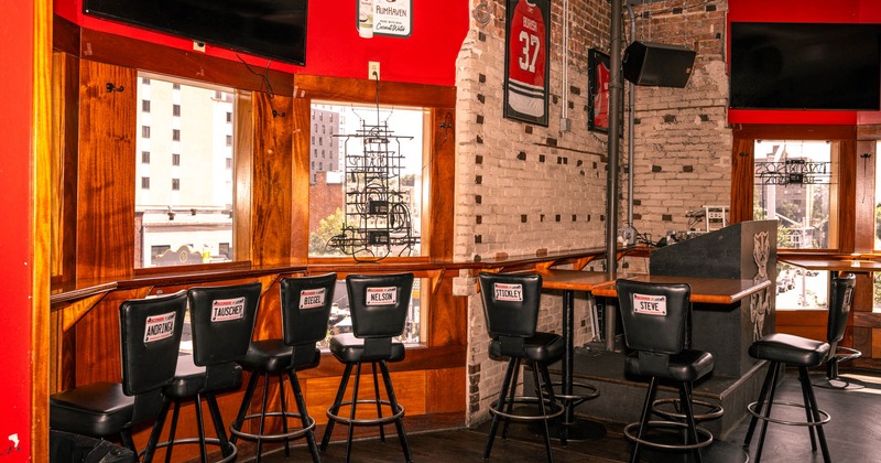 Interior, high seating ledge table with bar stools by the window, TV sets on the walls