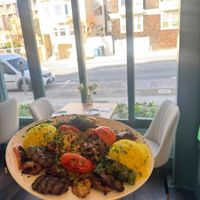 A plate of assorted grilled meats, yellow rice, and roasted veggies is held up in the restaurant.
