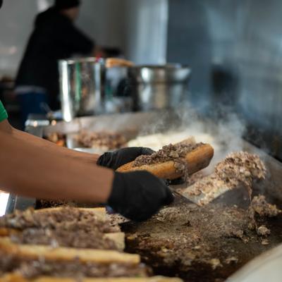 Cheesesteak sandwiches being prepared on a hot grill.