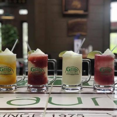 Frozen cocktails in glass mugs lined up on bar.