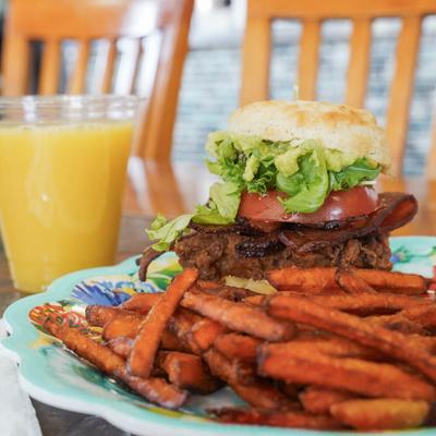 Fried chicken BLT sandwich on a biscuit with sweet potato fried and a glass of orange juice.