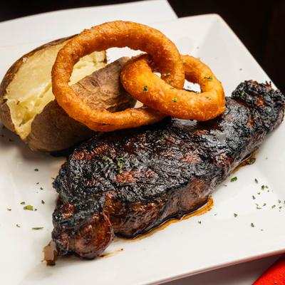 Char-grilled steak served with fried onion rings and a baked potato