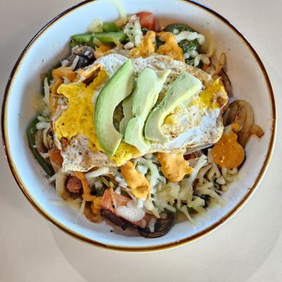 Breakfast bowl with avocado, fried eggs, cheese and various vegetables.