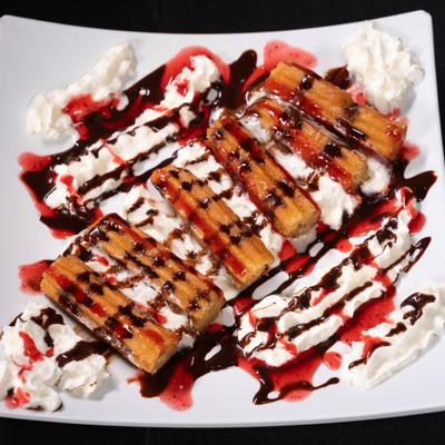 Churros drizzled with both chocolate and strawberry sauces, served with whipped cream.