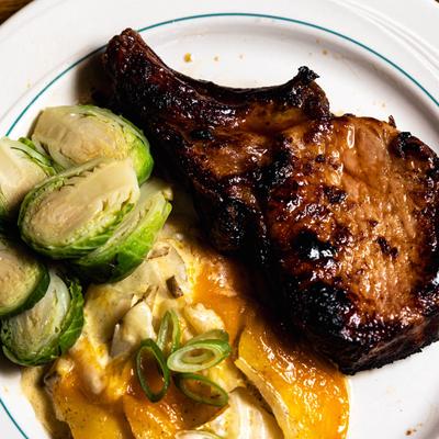 Bone-in pork chop served with Brussels sprouts and potato au gratin.