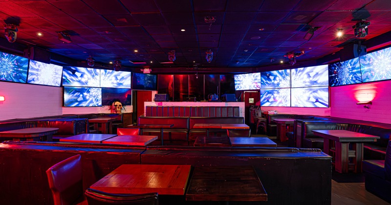 Nightclub interior with tables, leather seating and large screens displaying abstract visuals