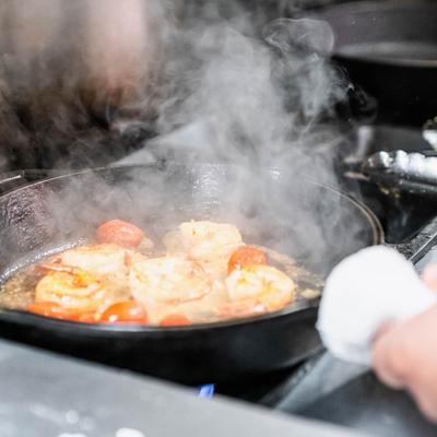 Shrimp and cherry tomatoes cooking in a cast-iron skillet, with steam rising.