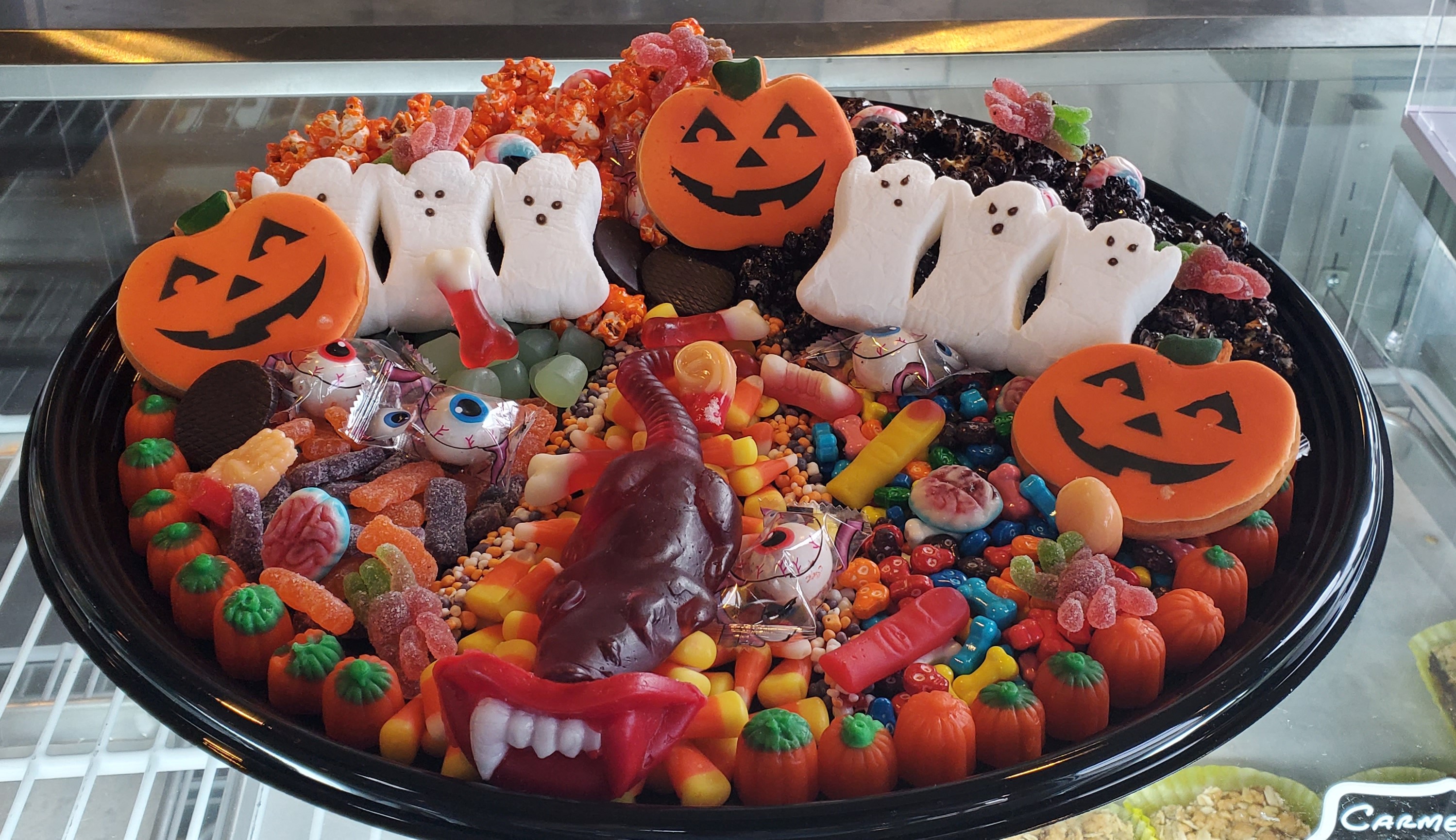 A round tray decorated with halloween candy including marshmallow ghosts, a gummi rat, and many other themed elements.