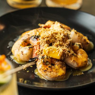 Seared shrimp with butter and shredded topping on a black plate.