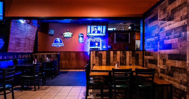 Interior of a dimly lit bar with rustic wooden decor, tables, chairs, a TV