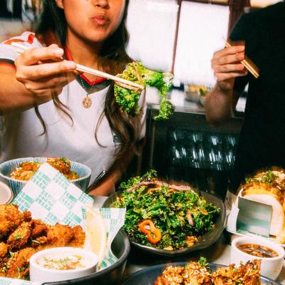 A person using chopsticks to pick up food from a spread of dishes.