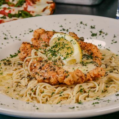 Chicken piccata with spaghetti, lemon wedge, and herb garnish.