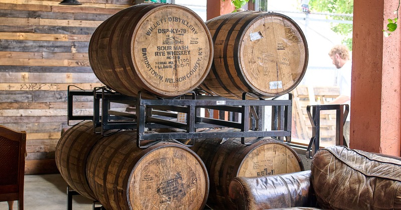 Stacked whiskey barrels beside leather couch and a wooden table