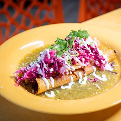 Flautas topped with shredded cabbage, crema, and cilantro, served over green salsa.