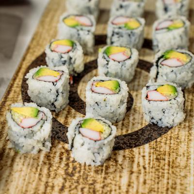 Sushi rolls with avocado and imitation crab rest on a board.