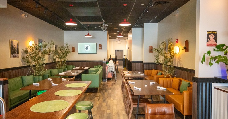 Interior of a restaurant with a bar counter, cushioned seating and wooden tables set with napkins