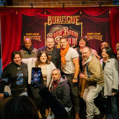 A cheerful group of people  posing for a picture in front of a red curtain backdrop poster.