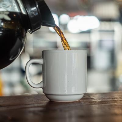Coffee being poured into a white mug on wooden table.