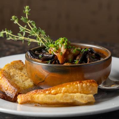 A bowl of mushroom stew served with bread and fresh thyme.