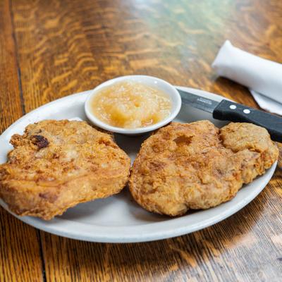Breaded and fried pork chops accompanied by a cup of applesauce.
