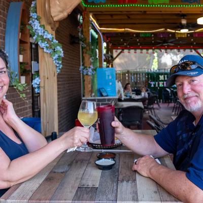 Two people clinging glasses with drinks at the table.