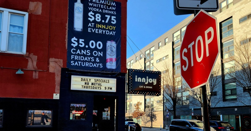 Innjoy bar exterior with a drink specials sign and a stop sign on a city street