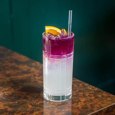 Layered cocktail featuring a vibrant purple top layer and cloudy citrus lemonade base.