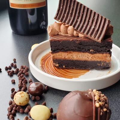 Chocolate dessert with layered cake on a white plate, next to a wine bottle.