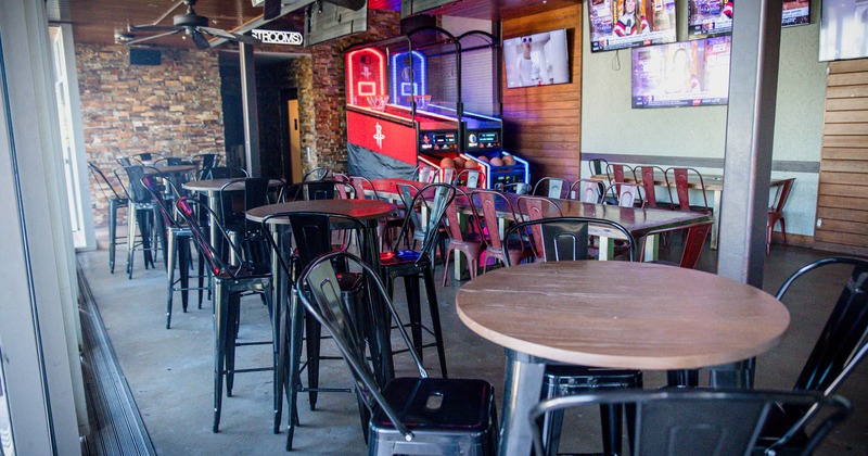 Interior, bar tables with bar chairs and a basketball arcade machine in the back