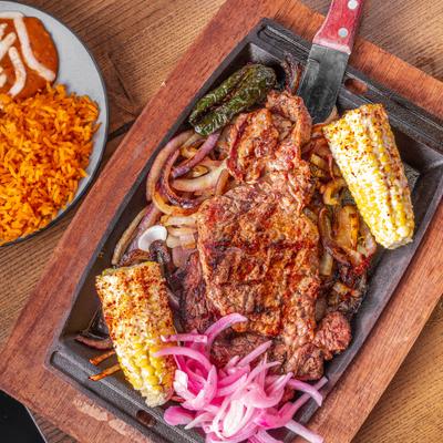 Carne Asada with sides of corn on a cob, rice and beans.