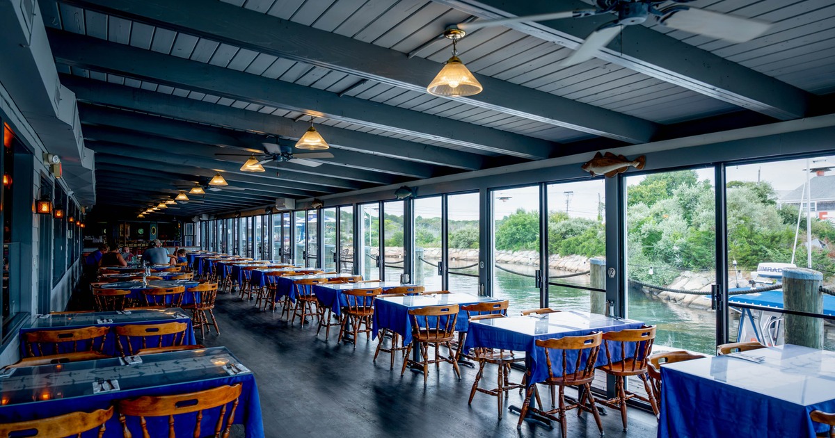 A coastal restaurant interior with wooden flooring, beamed ceilings, and large windows
