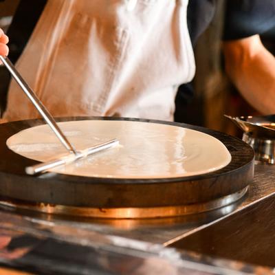 A person cooking crepe on a round griddle.