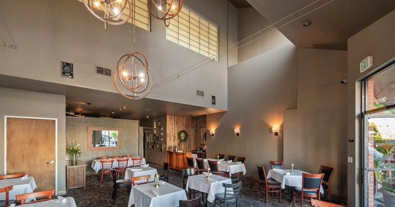 A modern restaurant interior with high ceilings, chandeliers, white tablecloths
