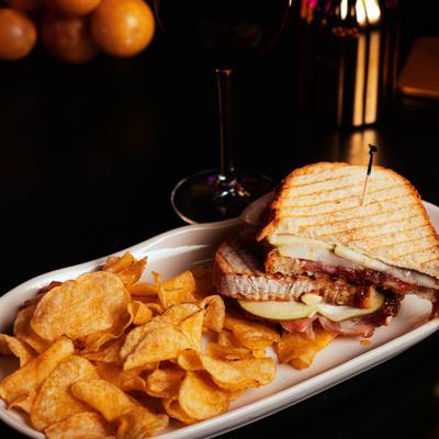 Ham, cheese, and bacon panini served alongside potato chips.