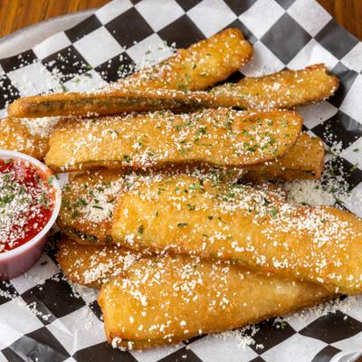 Fried zucchini sticks with grated Parmesan and marinara sauce on checkered paper.