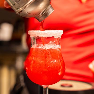 Cocktail being strained from the shaker into a rimmed glass.