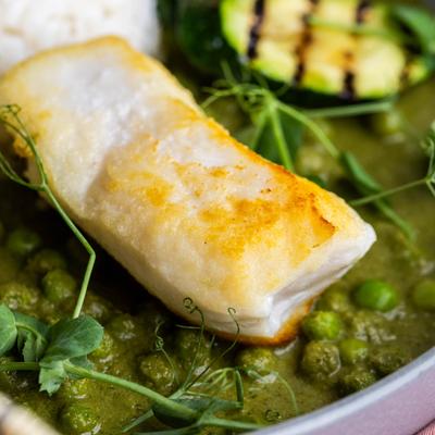 Close-up of a white fish filet over green peas sauce with fresh herbs.