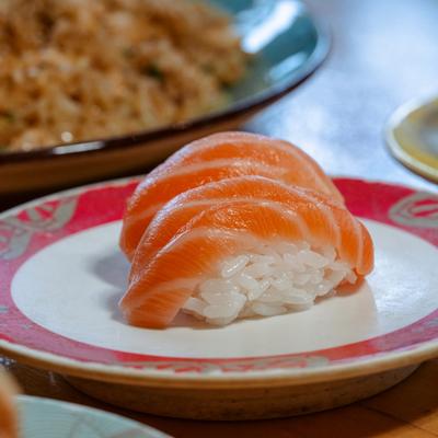 Salmon nigiri on red patterned sushi plate.