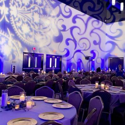 Room illuminated by monogram light for an event, set tables and chiars.