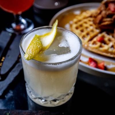 Peaches and Cream cocktail in a rocks glass, garnished with a lemon peel.