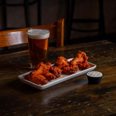 A plate of spicy chicken wings served with ranch dip and a pint of beer.