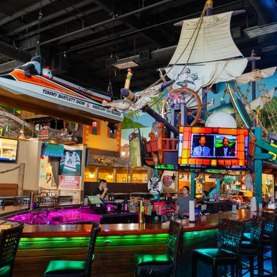 Interior of a bar with a racing boat hanging from the ceiling and pirate ship decor.