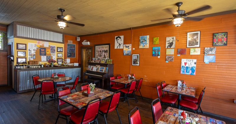 Interior of a cozy restaurant with orange walls, red chairs, and a mix of tables
