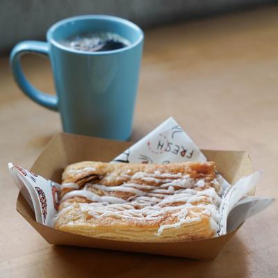 Chocolate bear claw in a paper tray and a coffee on a table.